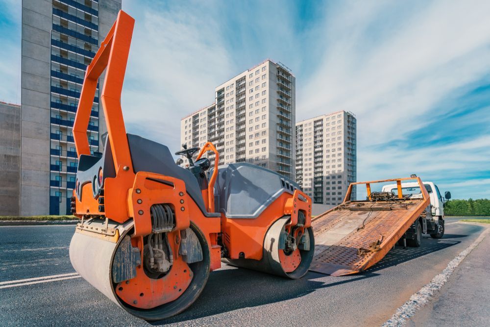 A Construction Vehicle is on the Side of the Road Next to a Truck — Dino's Bobcat–Bitumen & Excavator Hire in Kingaroy, QLD