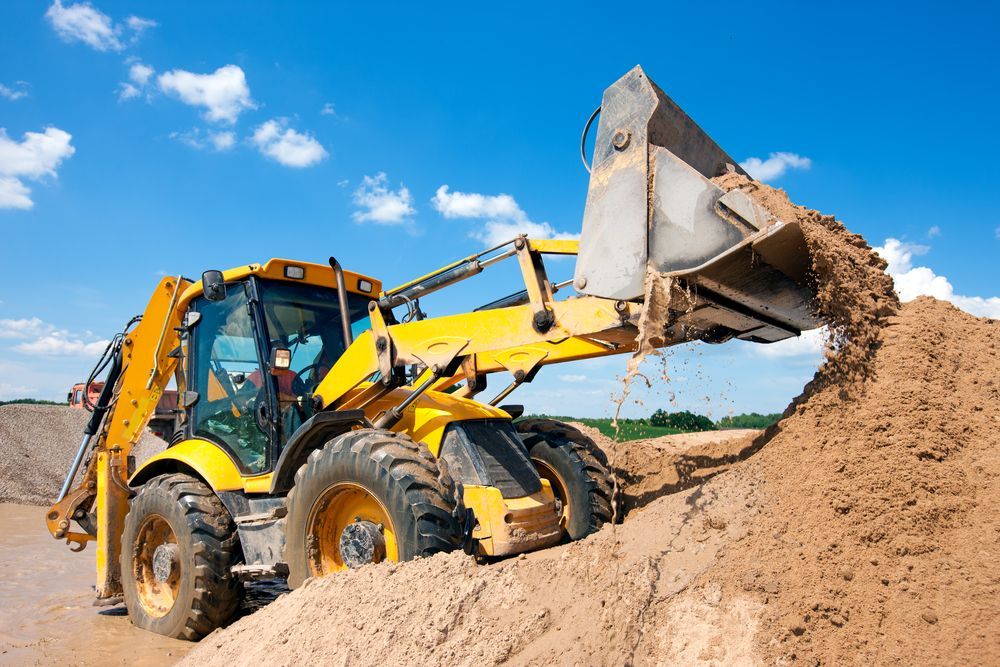 A Yellow Bulldozer is Loading Dirt Into a Pile — Dino's Bobcat–Bitumen & Excavator Hire in Gayndah, QLD
