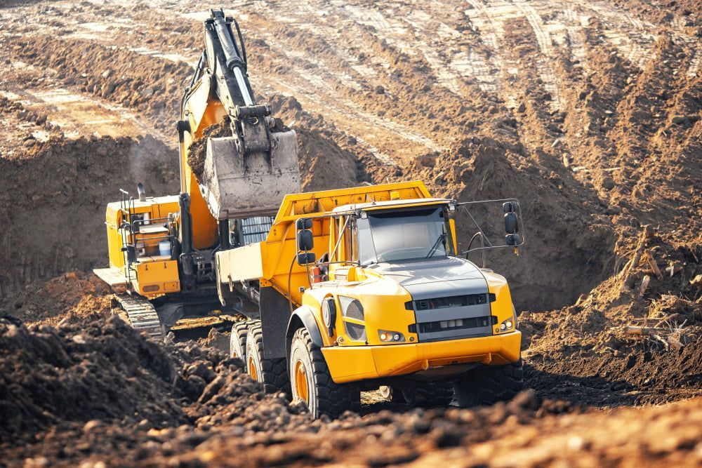 A Yellow Dump Truck is Being Loaded With Dirt by an Excavator — Dino's Bobcat–Bitumen & Excavator Hire in Kingaroy, QLD