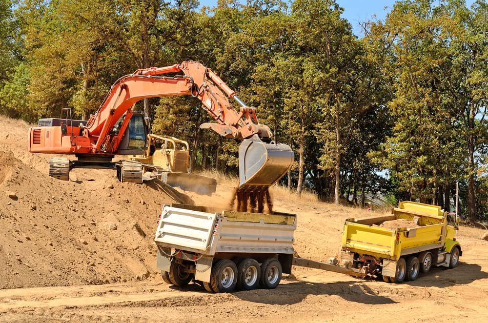 An Excavator is Loading Dirt Into a Dump Truck — Dino's Bobcat–Bitumen & Excavator Hire in Gayndah, QLD