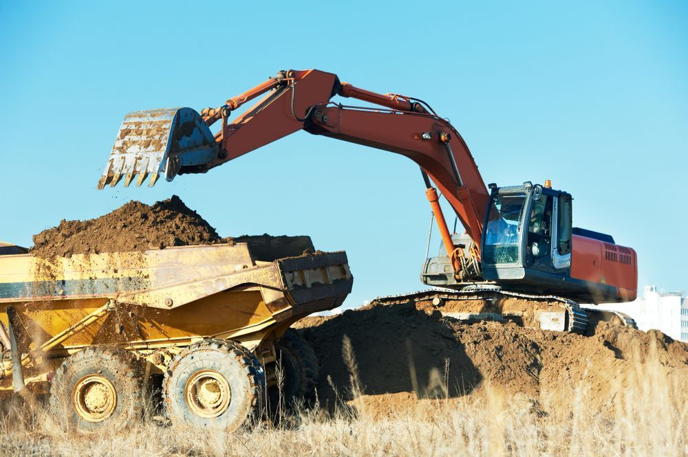 An Excavator is Loading Dirt Into a Dump Truck — Dino's Bobcat–Bitumen & Excavator Hire in Wondai, QLD