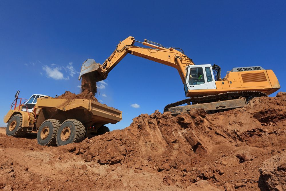 A Bulldozer is Loading Dirt Into a Dump Truck — Dino's Bobcat–Bitumen & Excavator Hire in Cushnie, QLD