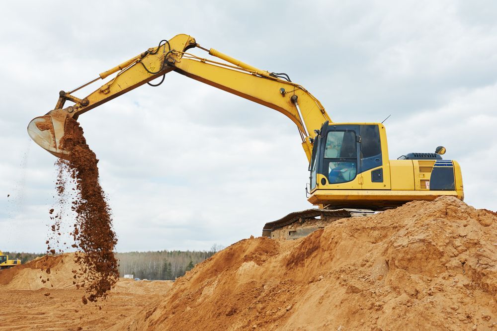 A Yellow Excavator is Pouring Dirt Into a Pile of Dirt — Dino's Bobcat–Bitumen & Excavator Hire in South Burnett, QLD