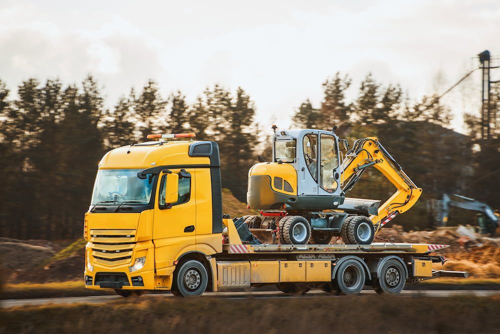 A Tow Truck is Carrying a Yellow Excavator on a Flatbed Trailer — Dino's Bobcat–Bitumen & Excavator Hire in Cushnie, QLD