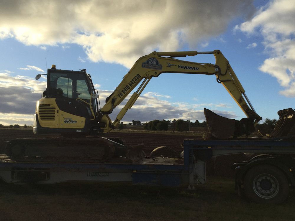 A Yellow Excavator is on the Back of a Truck — Dino's Bobcat–Bitumen & Excavator Hire in Cushnie, QLD