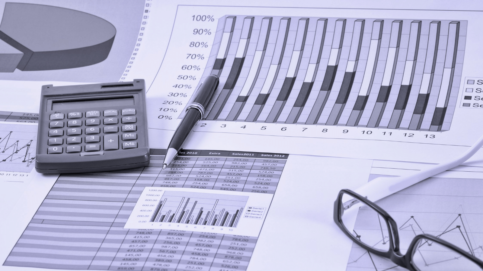 Desk with calculator, pen, charts, and eyeglasses beside financial graphs and reports
