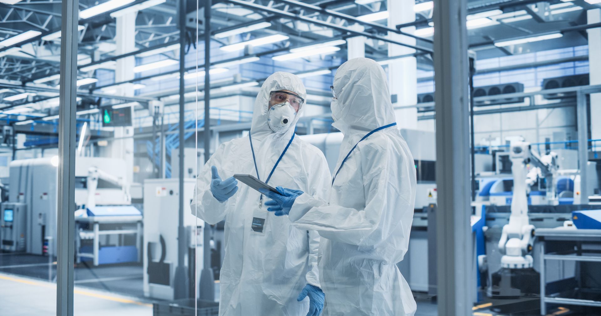 Two lab workers in protective suits discussing a tablet in a clean, high-tech laboratory
