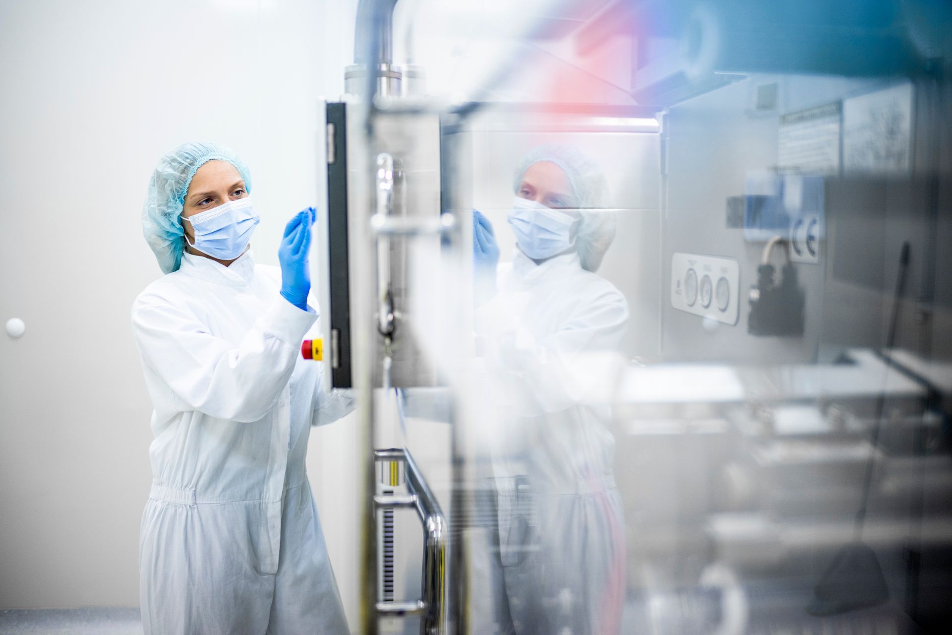 Lab technician in white protective suit and blue gloves inspecting a lab chamber door