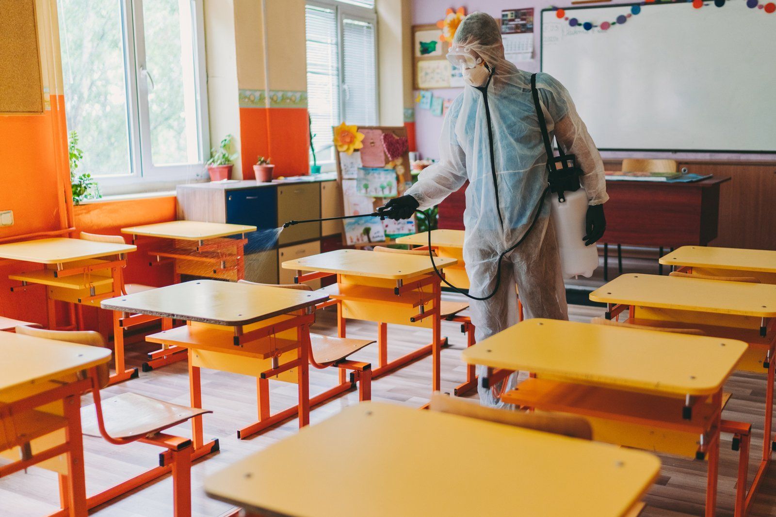 Person disinfecting desks in a colorful classroom with orange and yellow furniture
