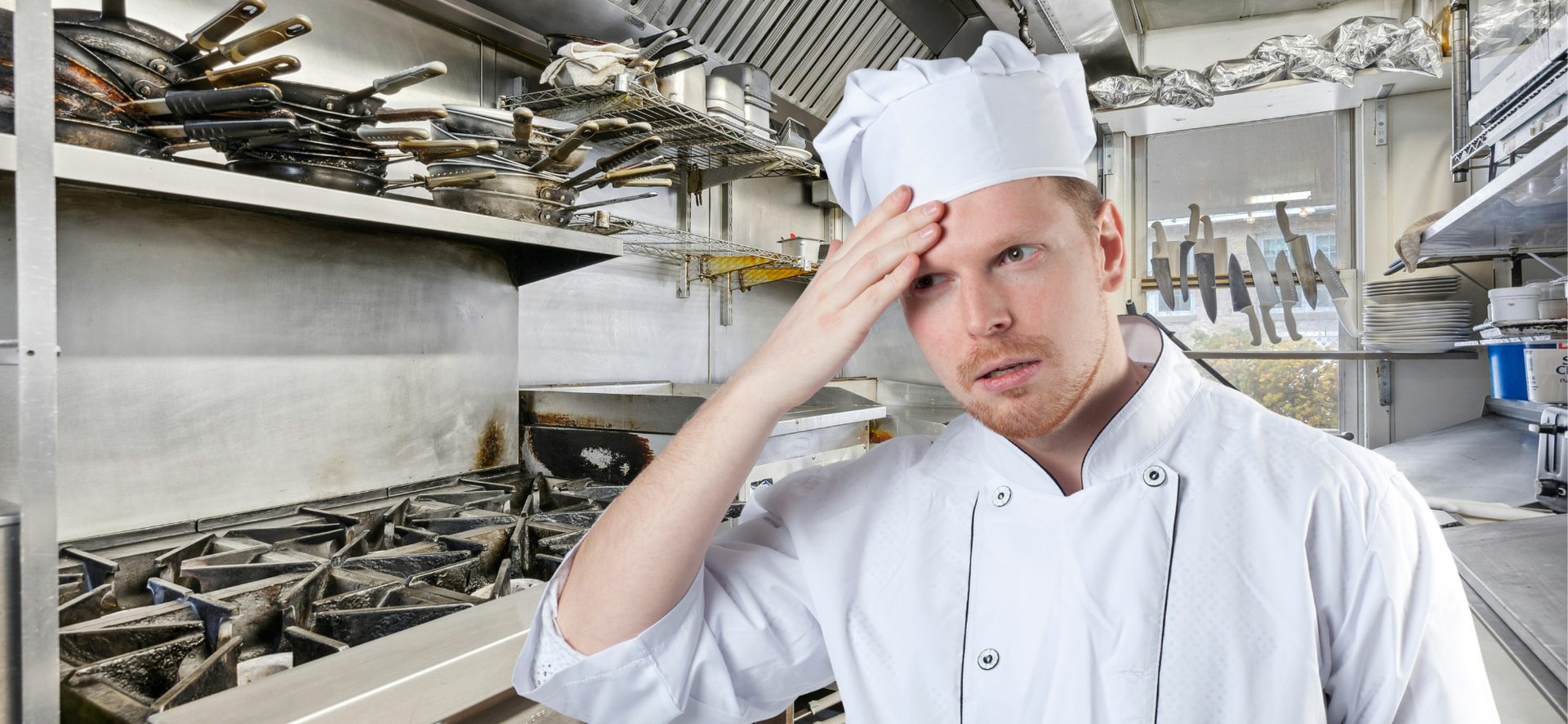 Chef in white uniform holding his forehead in a busy commercial kitchen with stainless steel equipment