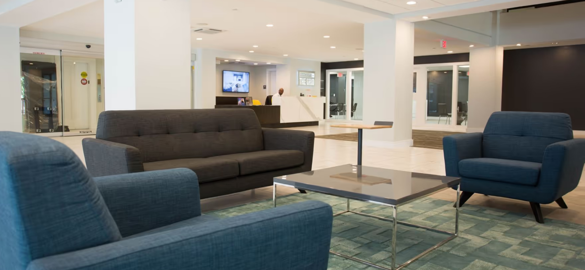 Modern living room with blue and dark gray sofas, glass coffee table, and bright open interior