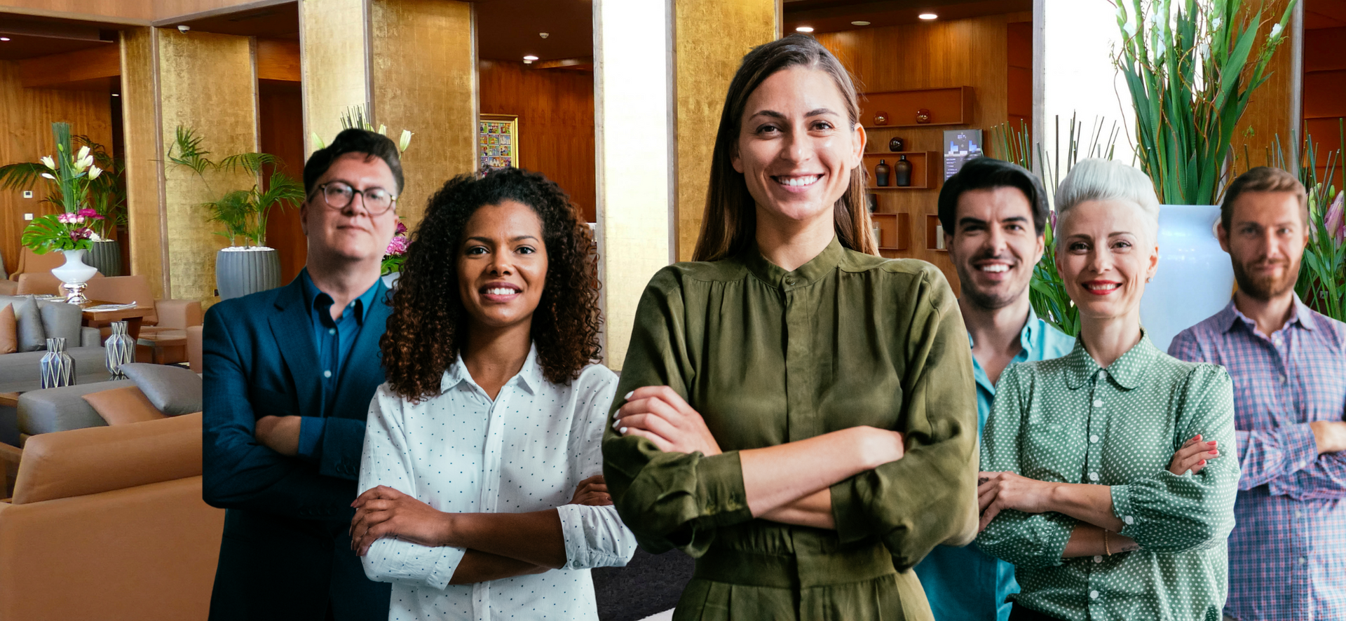 Five colleagues standing together in a modern office lobby, smiling with arms crossed