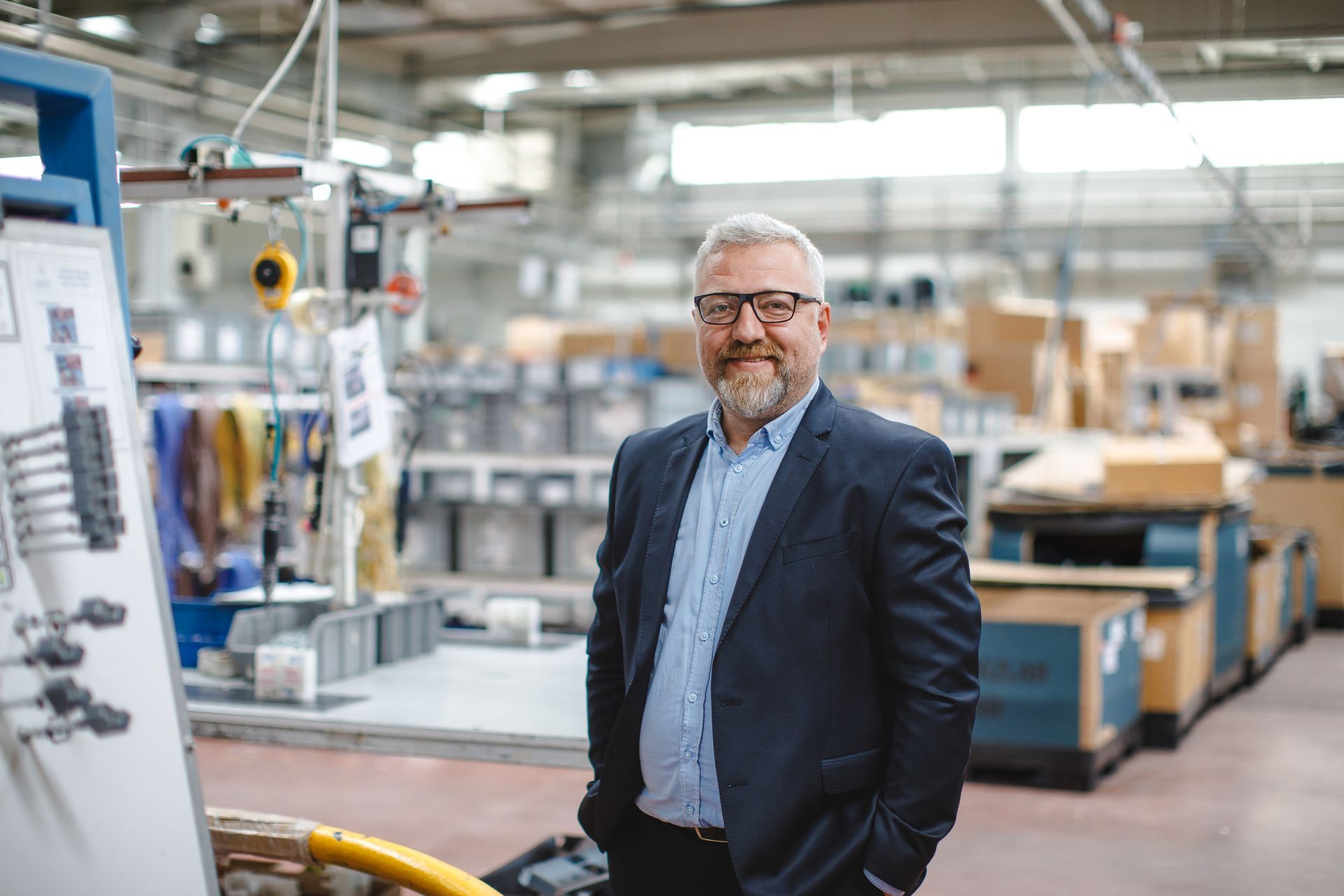 Man in a suit standing in a factory workshop with machinery and worktables in the background