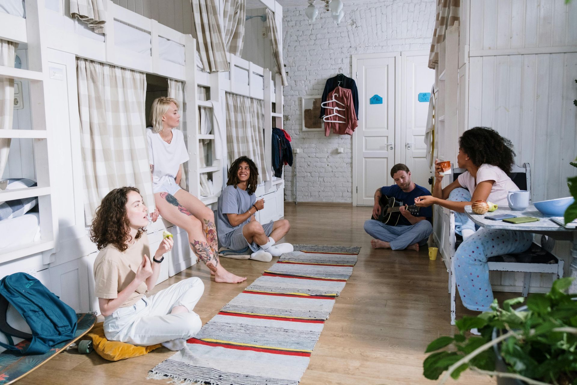 People sitting and chatting in a bright hallway with rugs, chairs, and potted plants