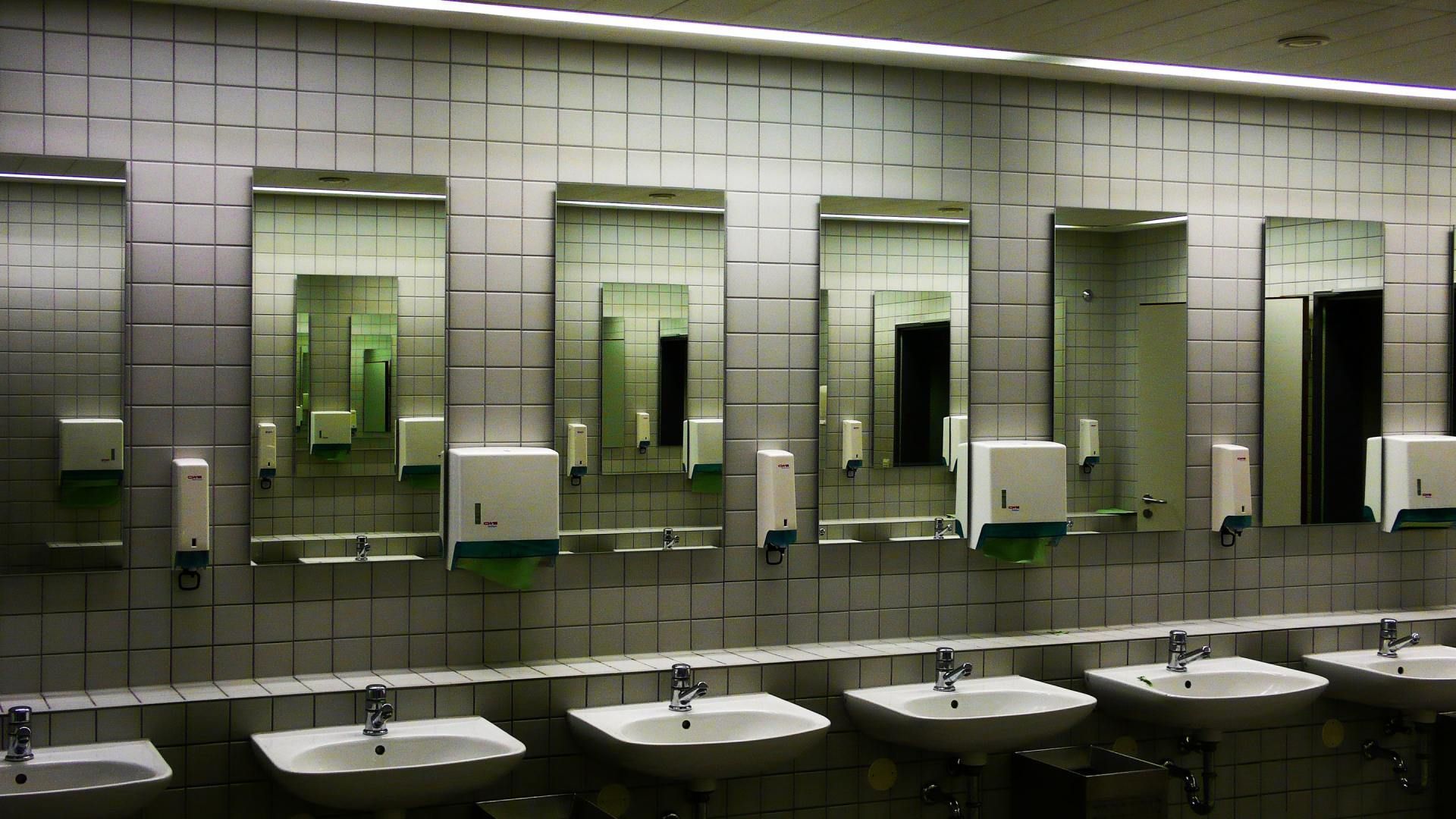 Row of sinks and mirrors in a tiled public restroom with greenish lighting