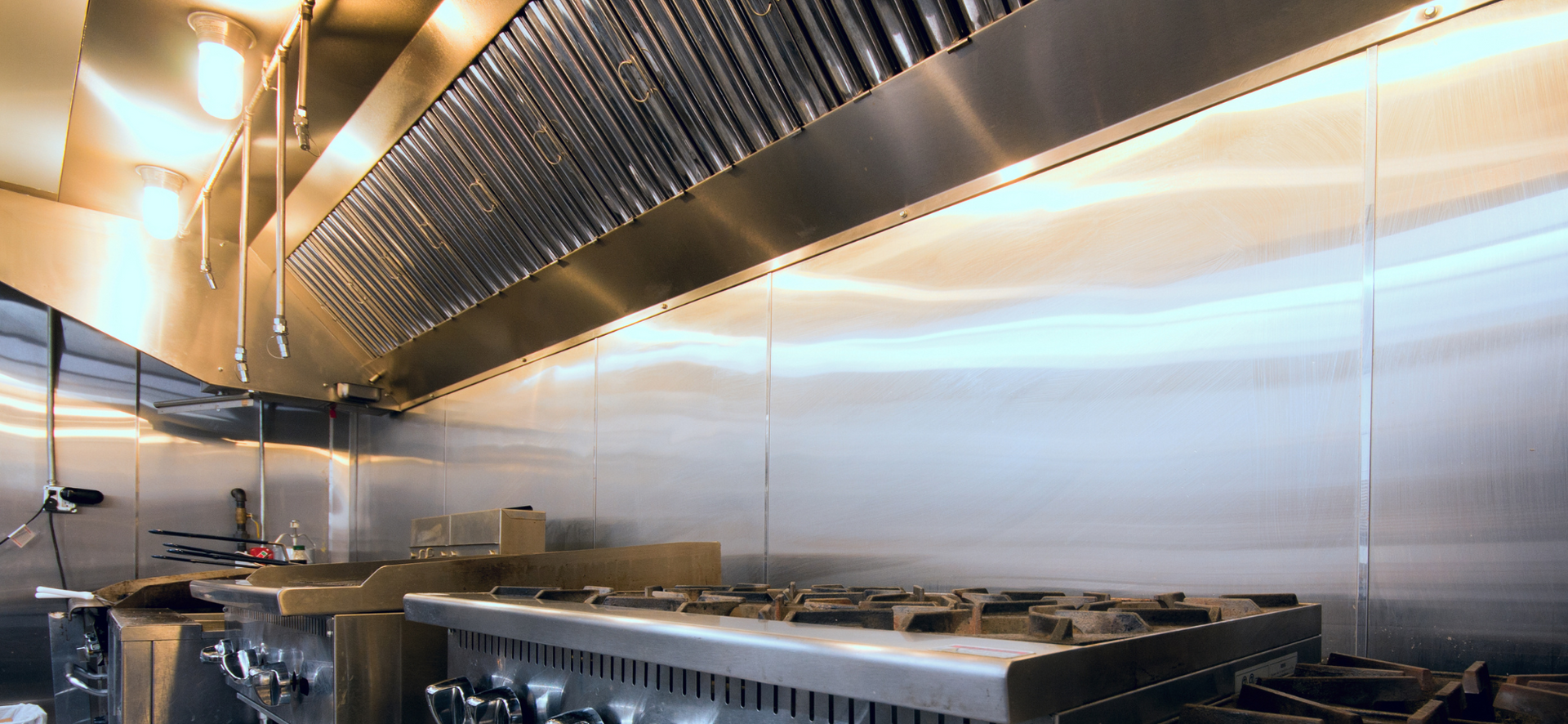 Commercial kitchen line with stainless steel counters, stove, and large exhaust hood