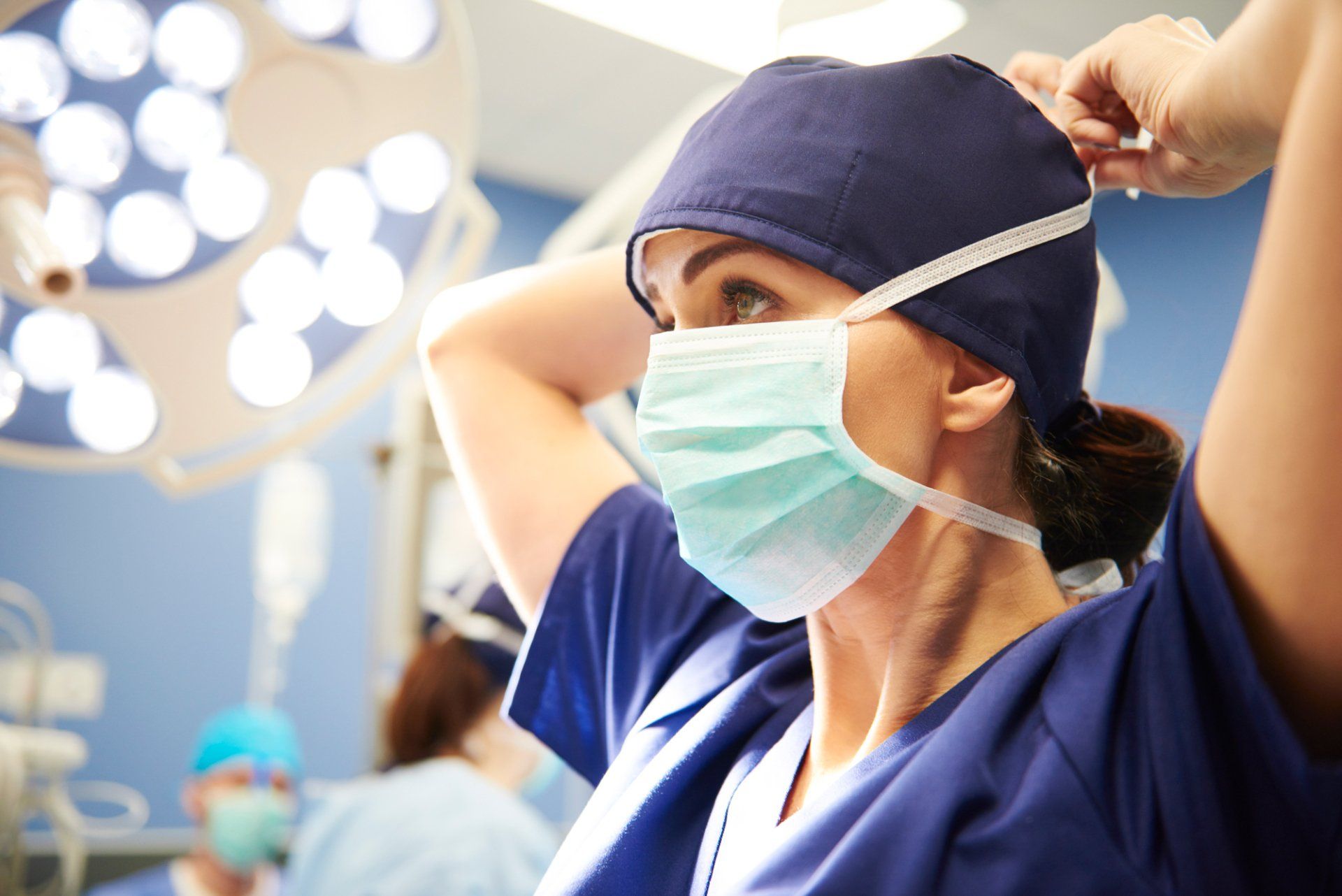 Healthcare worker putting on surgical cap and mask in operating room