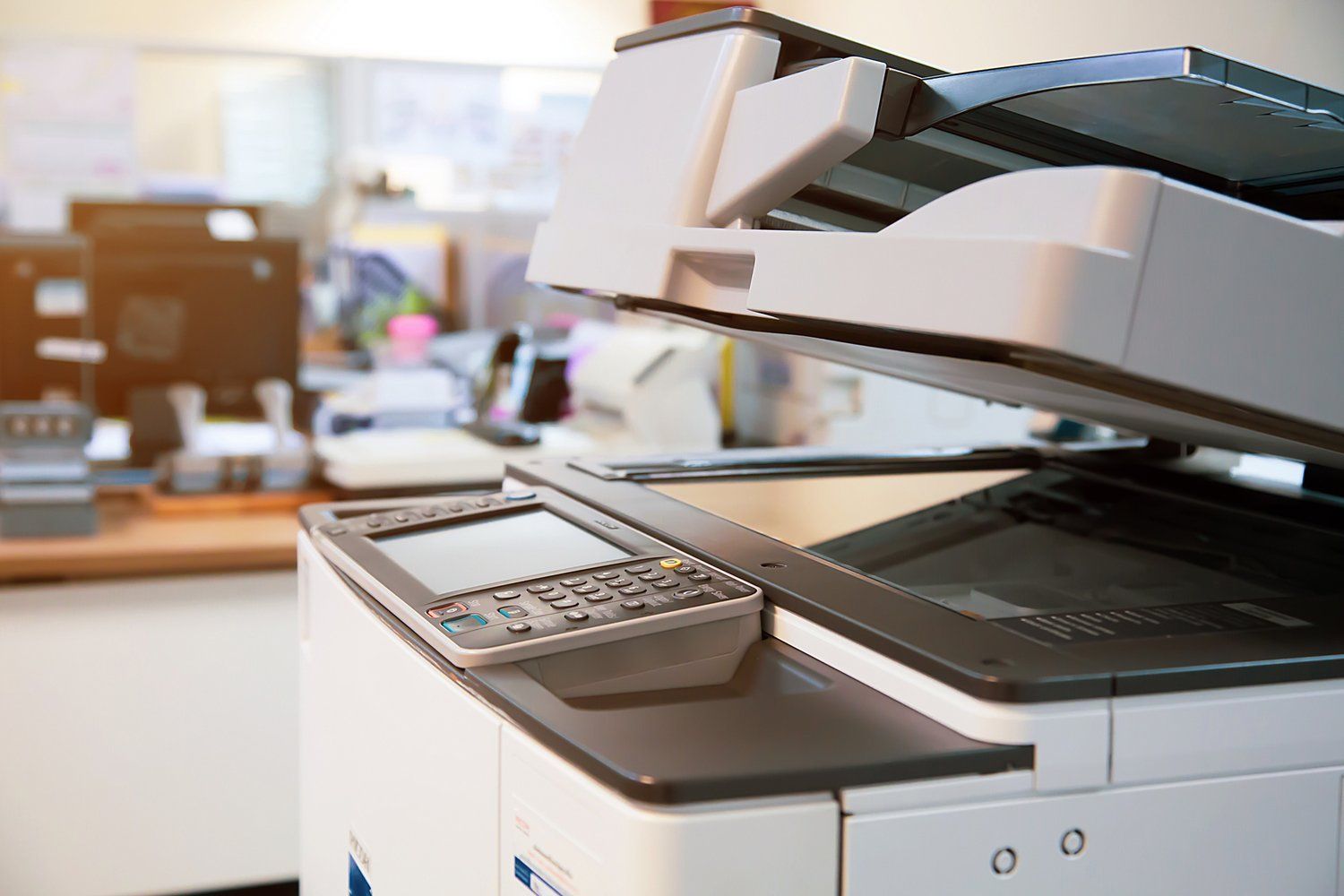 Office copier and printer in a bright workspace, with paper tray and control panel visible.