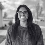 Smiling woman in glasses and sweater standing outdoors in a park-like setting