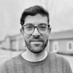 Portrait of a man with glasses and a beard, wearing a gray sweater outdoors