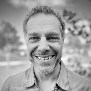 Smiling man in a checkered shirt outdoors, with a blurred background