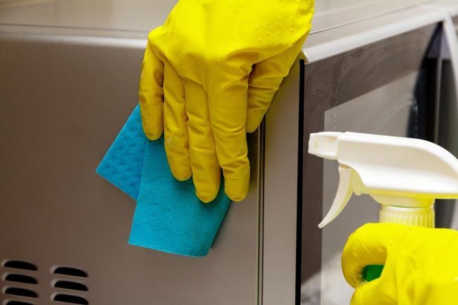 Gloved hands wiping a stainless steel surface with a blue cloth and spray cleaner