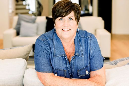 Woman with short brown hair smiles, wearing black shirt, against a dark background.