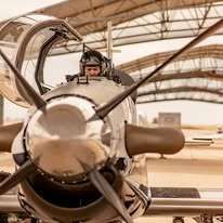 Pilot in cockpit of a silver propeller plane, preparing for flight.