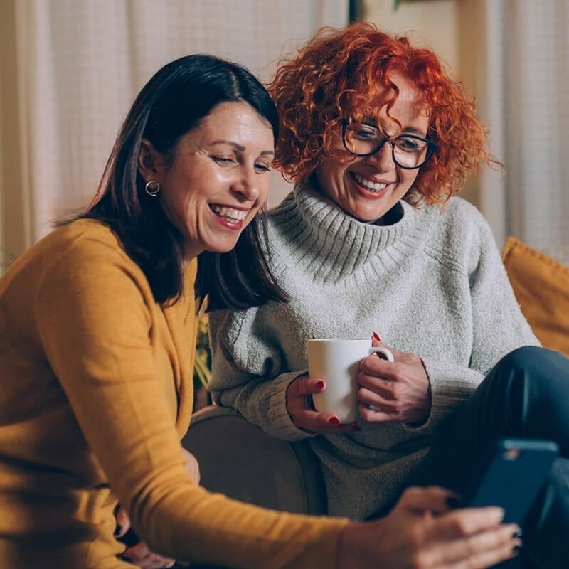 Two women are sitting on a couch looking at a tablet.