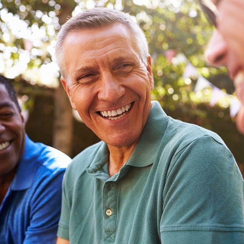 A man in a green shirt is smiling while sitting with two other men