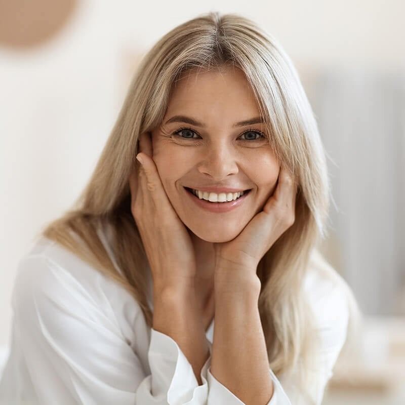 A woman is smiling with her hands on her face.