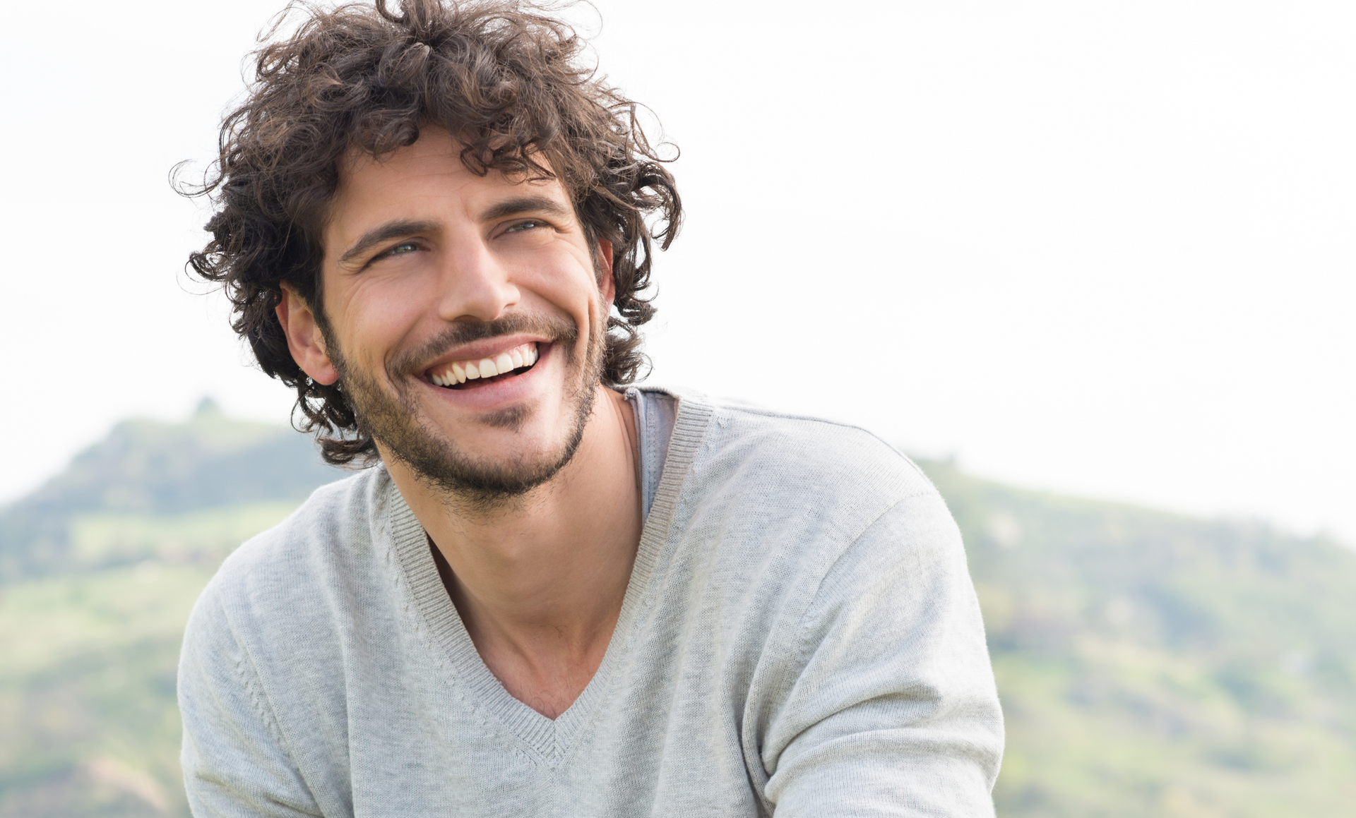 A man with curly hair and a beard is smiling.