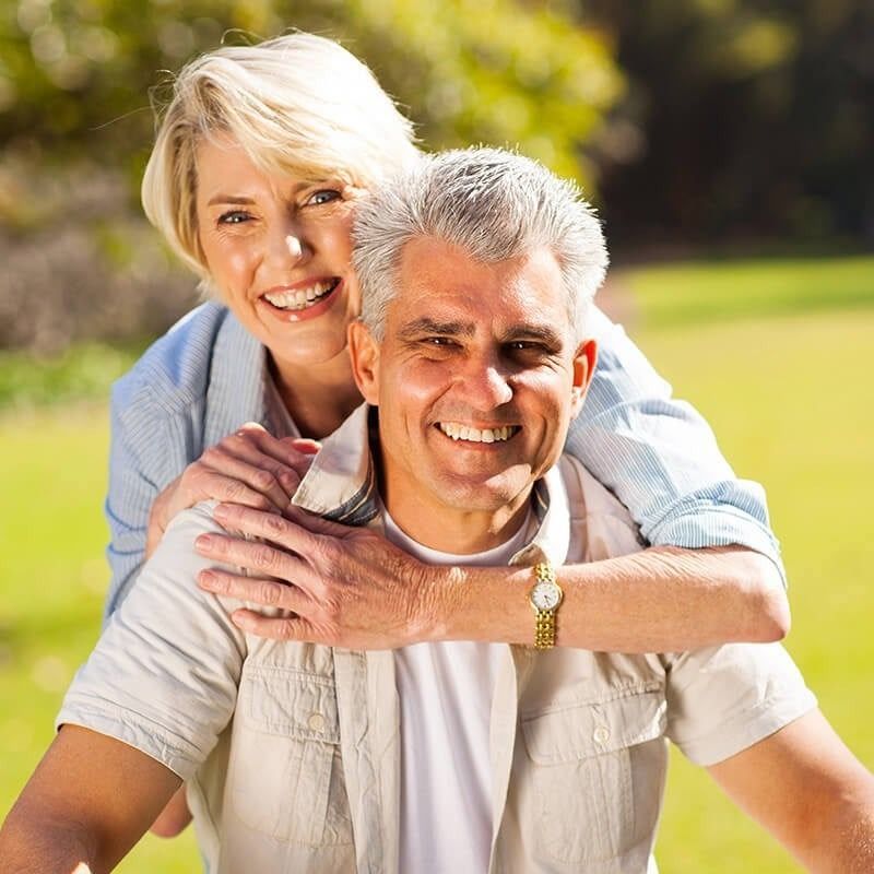 A man is carrying a woman on his back and they are smiling for the camera