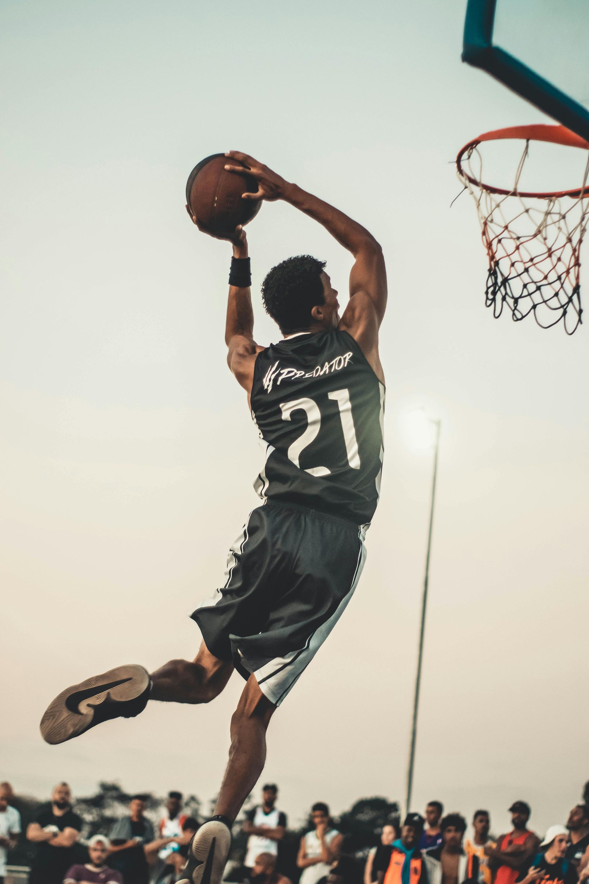 A man wearing a number 21 jersey is jumping in the air to dunk a basketball.