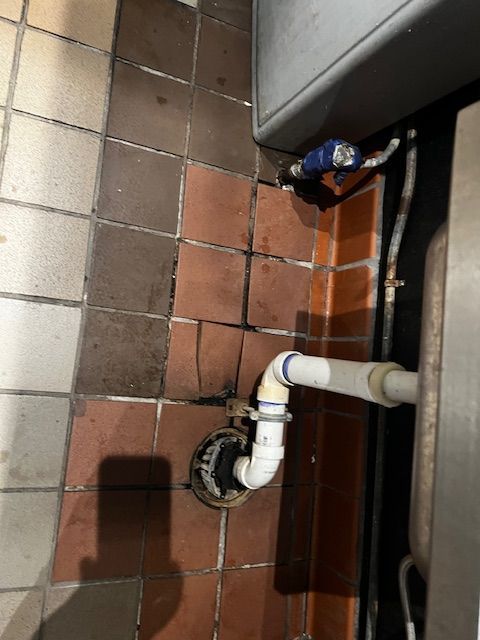 Bathroom floor with exposed white drain pipe and tiled wall beside a toilet.