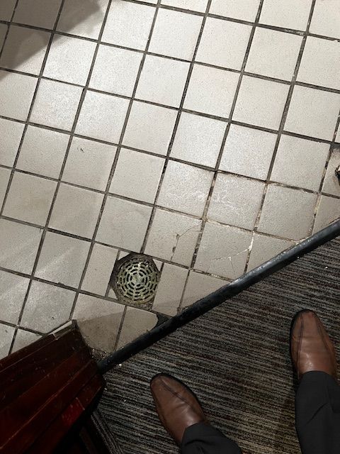 Tiled floor with a small floor drain and two brown shoes at the bottom edge
