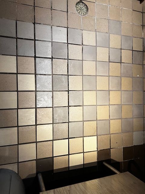 Tiled bathroom wall with a sink basin below and a small round clock above.
