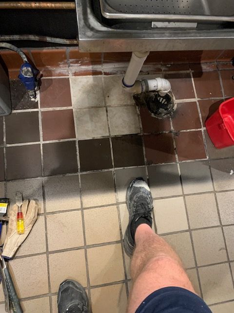 Person standing on tiled floor in a kitchen near a sink and trash can, with a red bucket nearby.