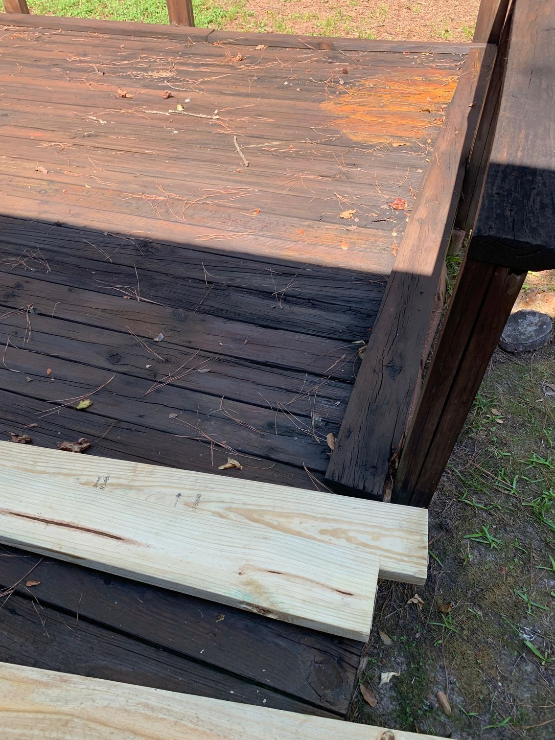 Weathered wooden bench or crate with a broken white plank in the foreground, outdoors on grass.