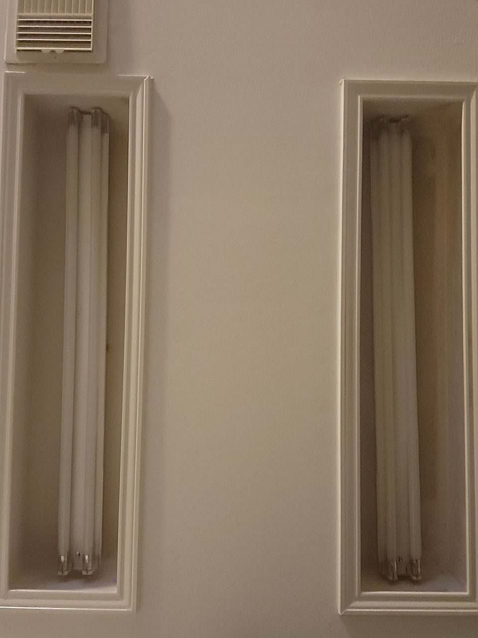 Close-up of two narrow fluorescent light fixtures on a beige wall.