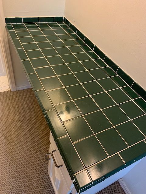 Green-tiled countertop with glossy surface, beside a beige wall and cabinet drawer handles