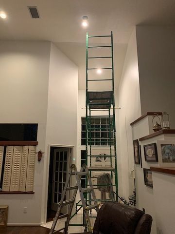 Ladders set up in a tall white room beneath a ceiling light, suggesting home maintenance or inspection
