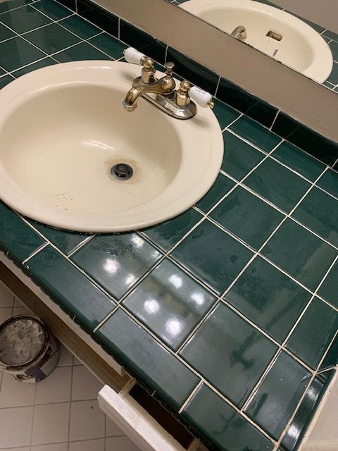 Bathroom sink with white basin and green tile countertop, seen at an angle with mirror reflection.