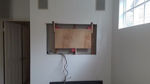 Partially installed wall-mounted TV frame with exposed cables in a sparsely furnished room