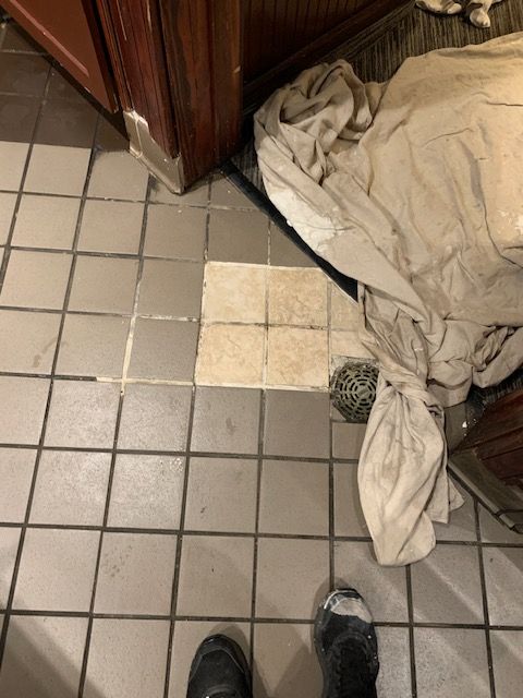 Tiled bathroom floor with a beige towel pile and a worn, discolored tile area near the doorway.