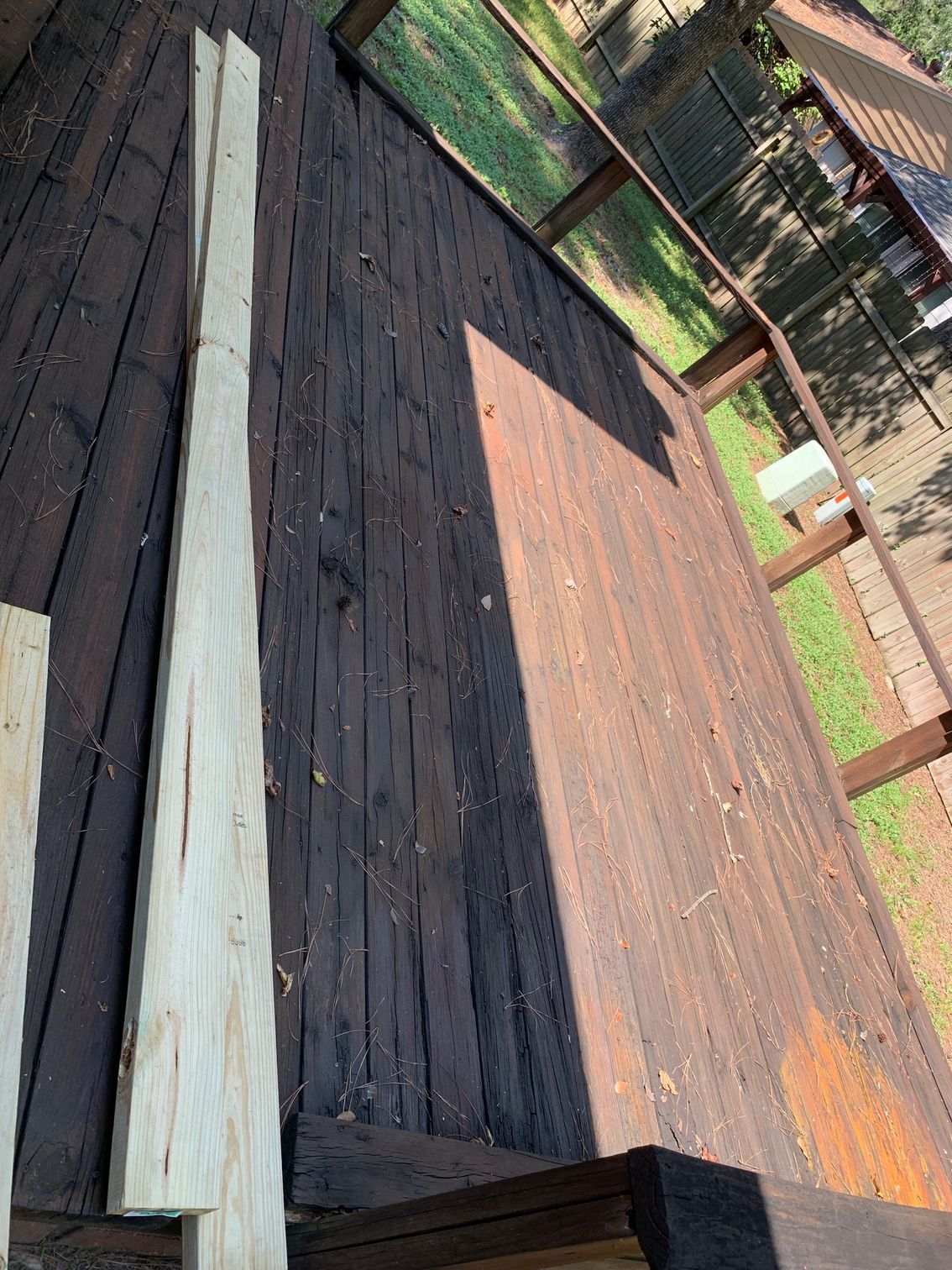 Wooden deck with long pale boards stacked beside a weathered fence in a sunny yard