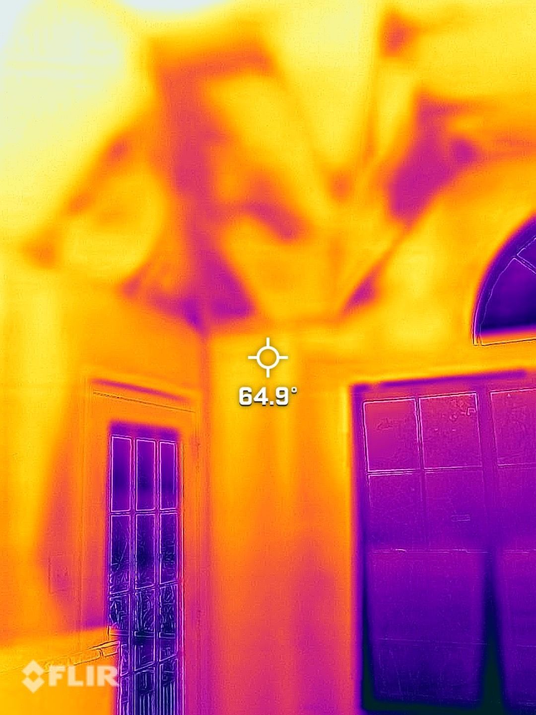 Thermal view of a house exterior with windows and a doorway, showing warm wall heat and cooler purple shadows