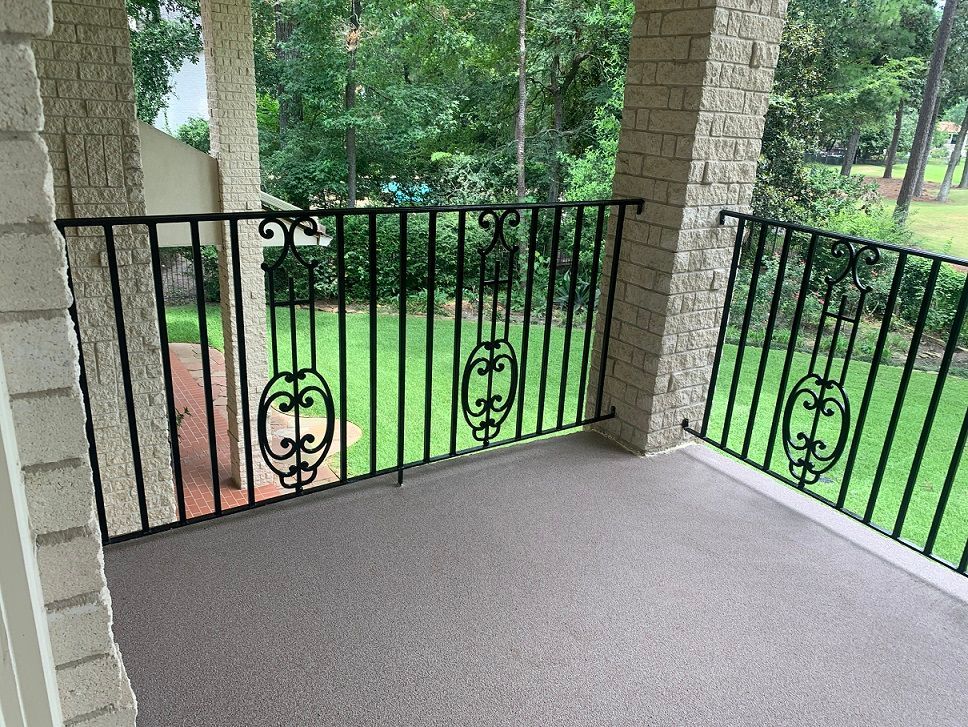 Covered patio with black wrought-iron railing, stone columns, and a green backyard view.
