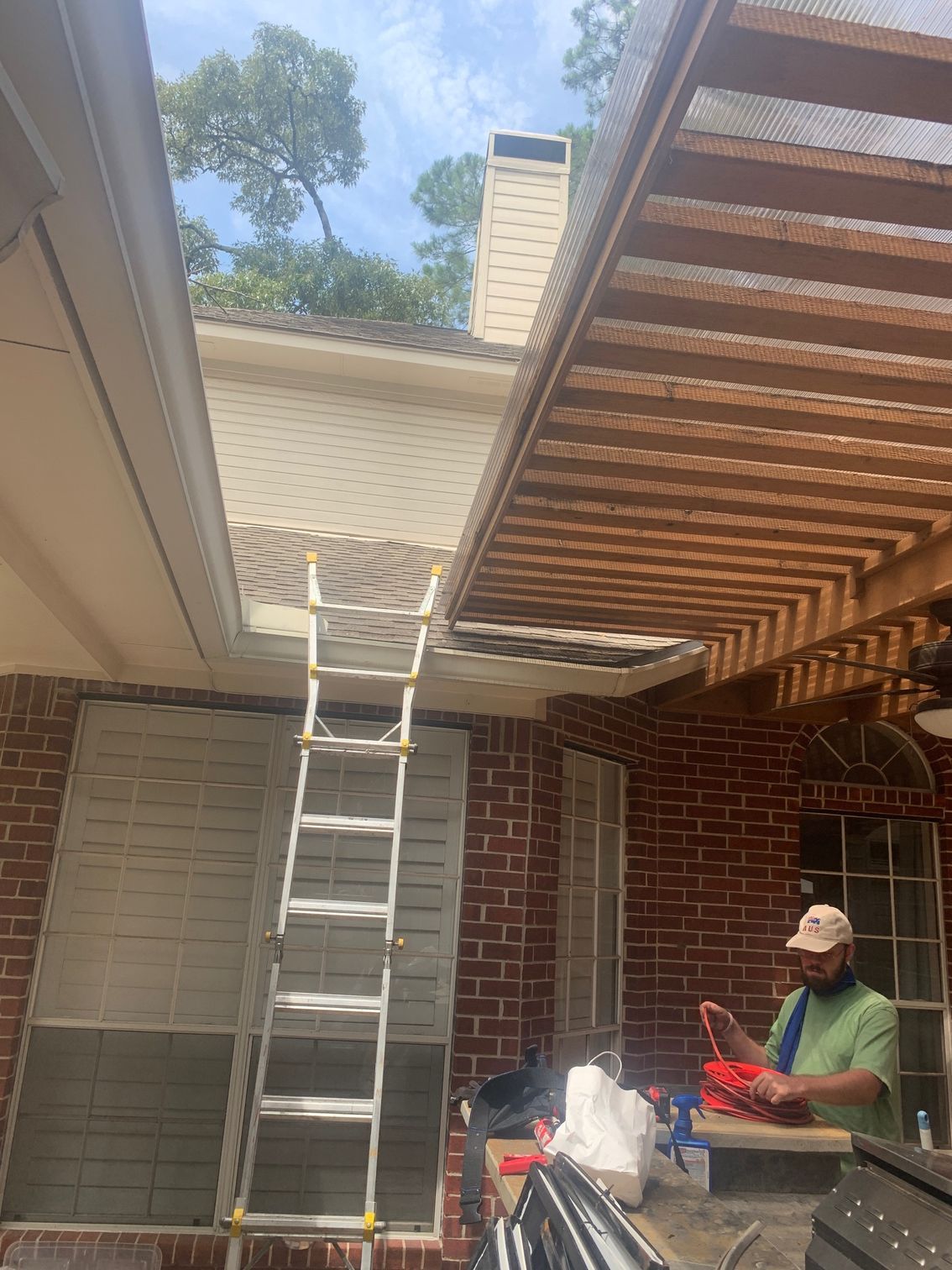 Extension ladder reaching a roof opening in a brick courtyard, with a worker standing below.