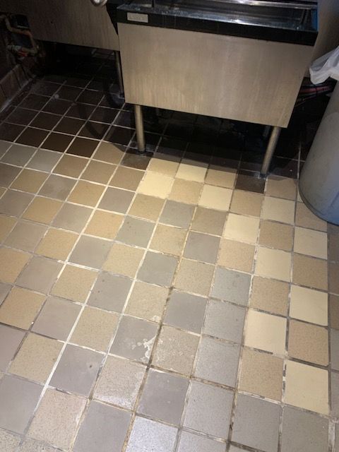 Tiled kitchen floor beneath stainless steel equipment, with one tile missing or damaged.
